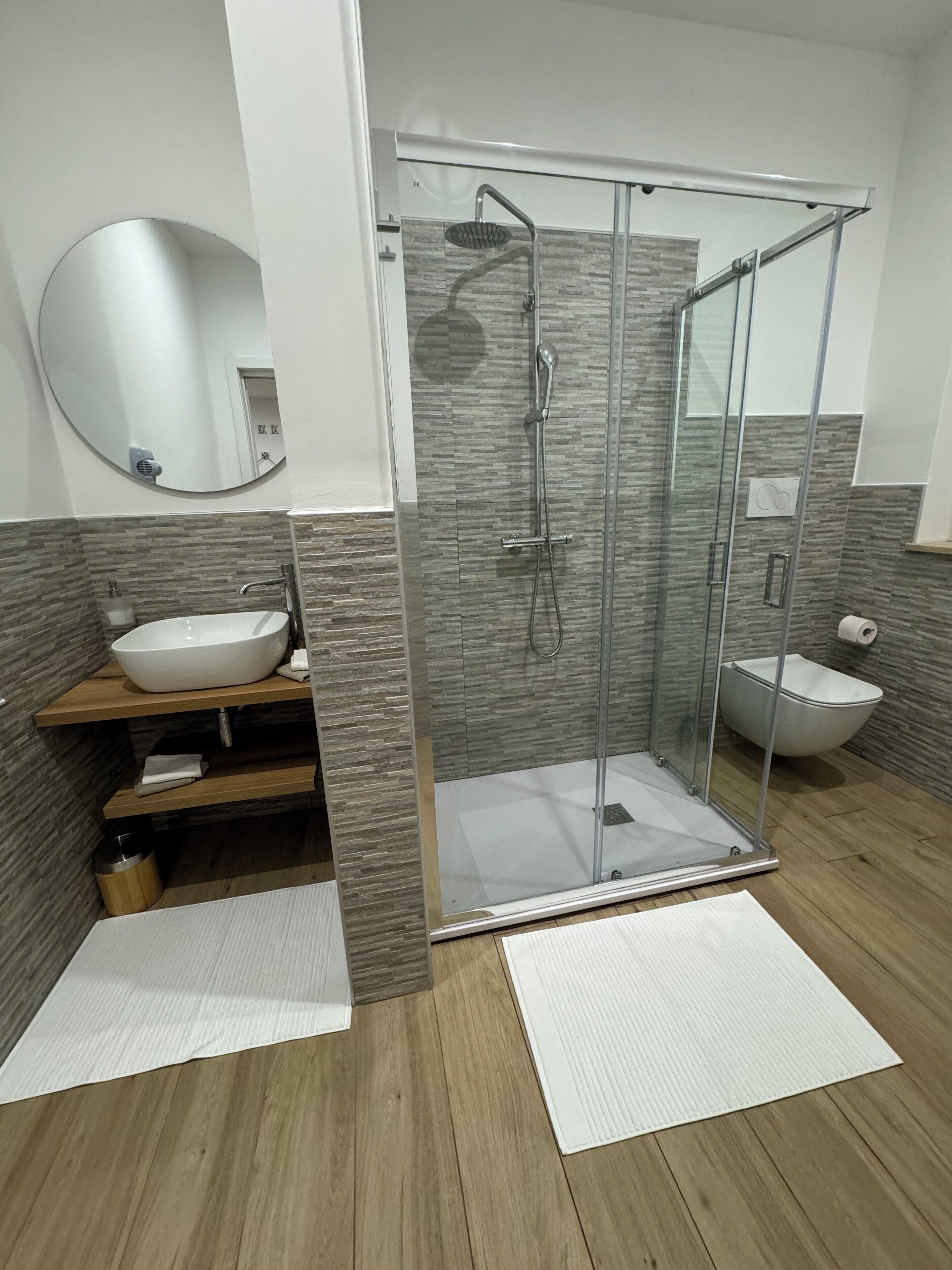 Ein modernes Badezimmer mit einer gläsernen Duschkabine, einem Holzbadezimmer-Möbel mit Waschbecken und einer weißen Toilette.