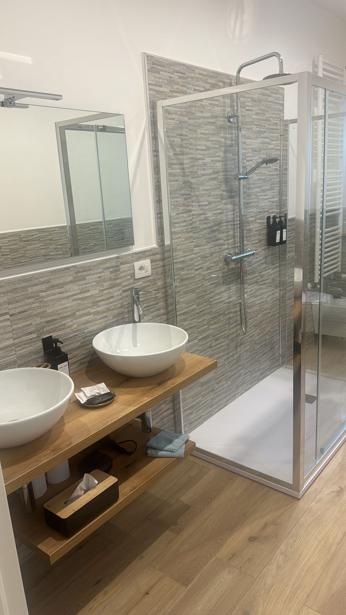 Un baño moderno con ducha de vidrio, un lavabo blanco grande y un mueble de tocador de madera.