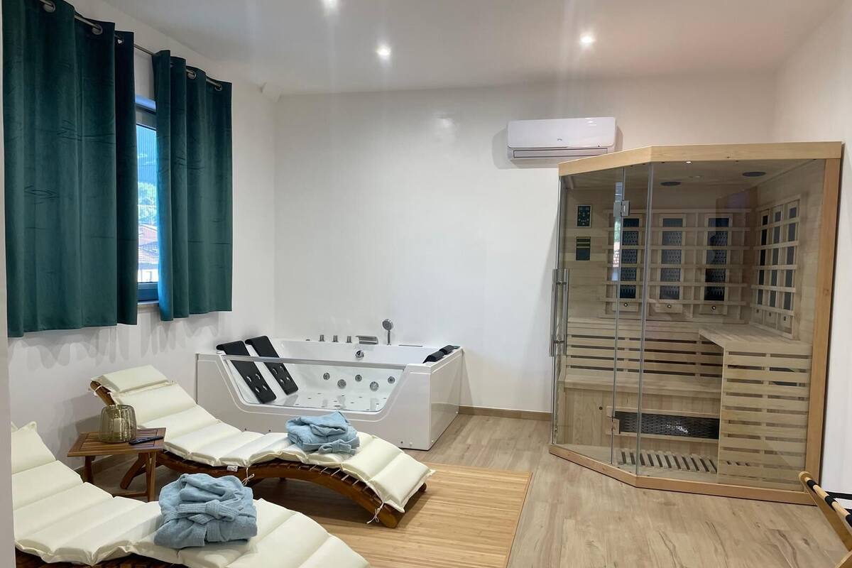 A spa room with a bathtub, two massage tables, and a wooden sauna.