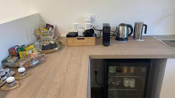 A compact kitchen with a built-in refrigerator, a coffee maker, a kettle, and various food items on the counter.