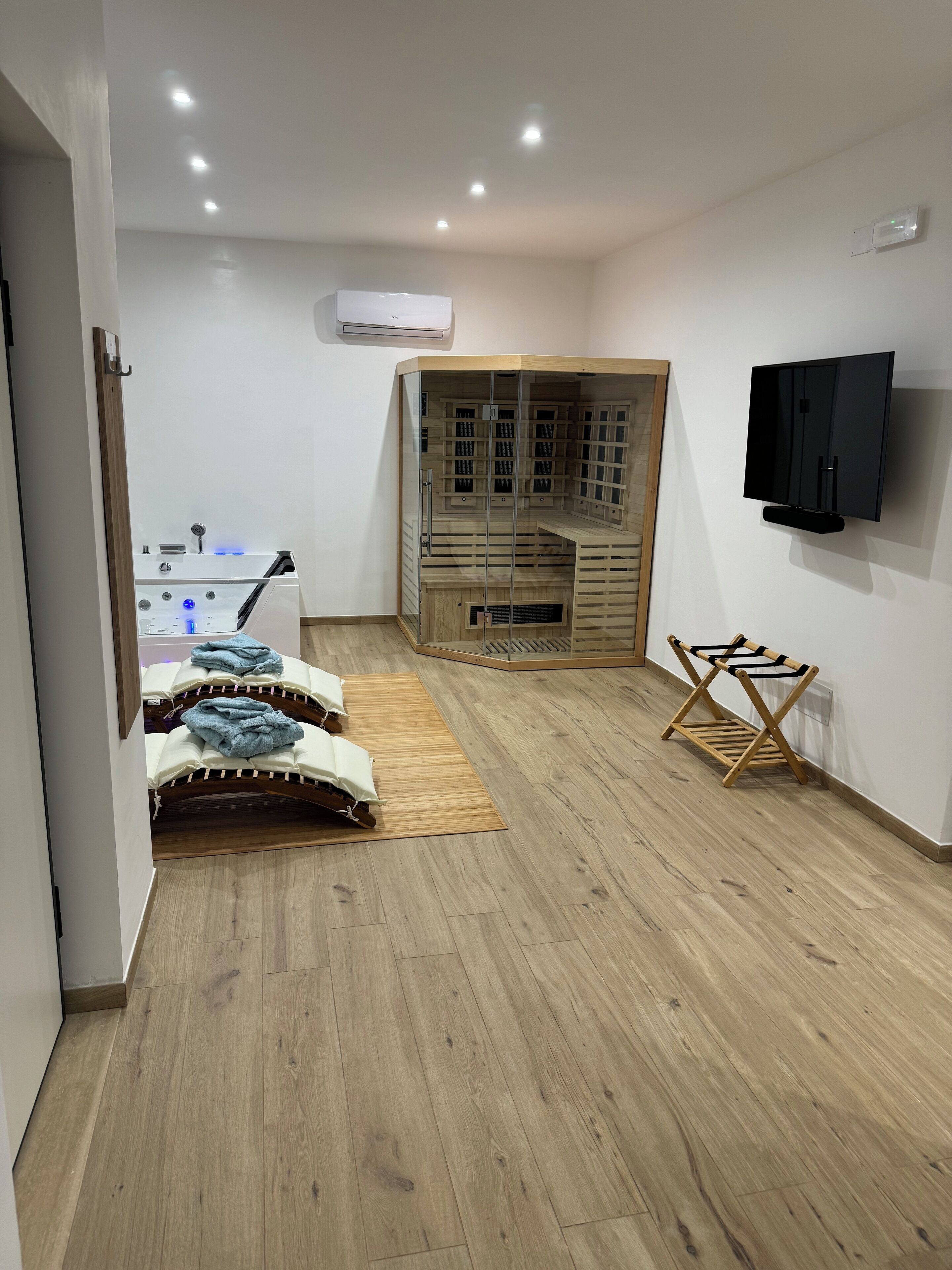 A room with a wooden floor, a sauna, a TV mounted on the wall, and a wooden drying rack.
