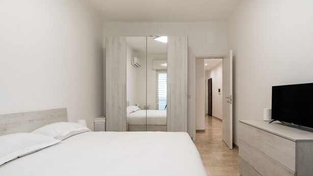 Una habitación de hotel moderna con una cama grande, un televisor, un aparador y un espejo.