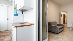 Una cocina moderna con armarios blancos, encimera de madera y una puerta corrediza de vidrio que da a una sala de estar con sofá gris y una silla blanca.