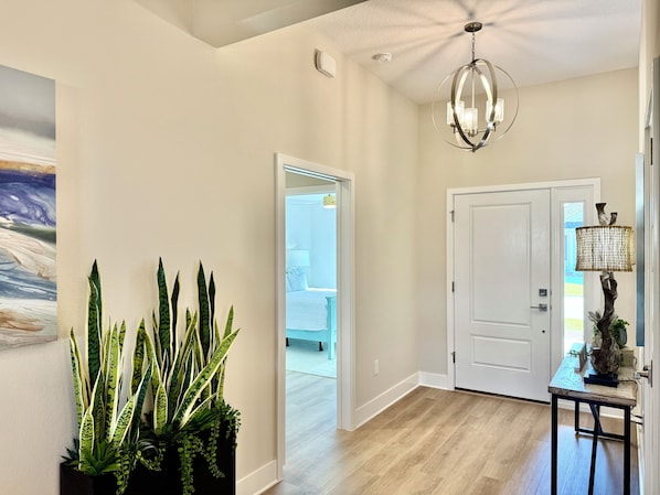 A hallway with a ceiling fan, a chandelier, a door, and a potted plant.