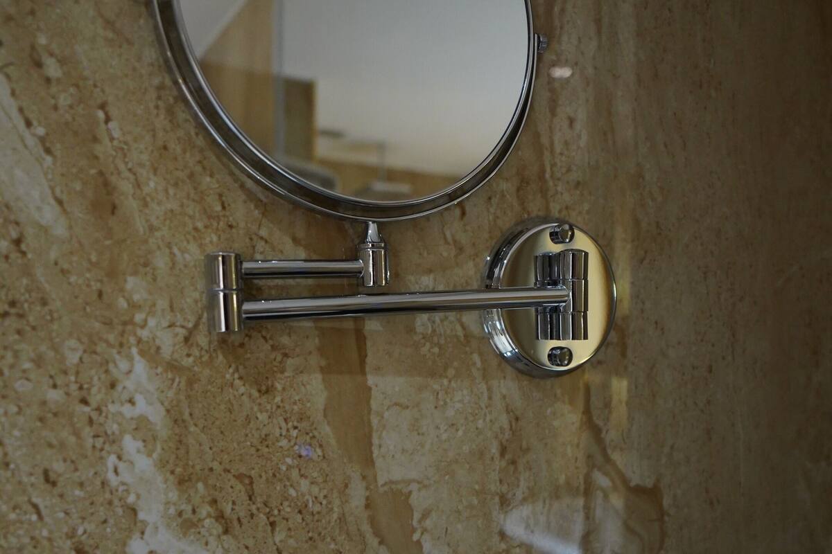 A bathroom with a marble wall, a round mirror, a towel rack, and two hand dryers.