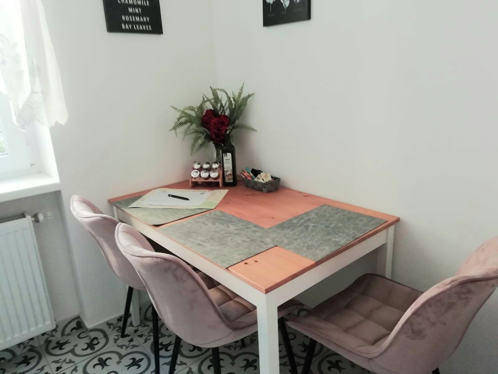 Un pequeño comedor con una mesa y cuatro sillas, un florero con flores, y un letrero en la pared que enumera los servicios de la habitación.