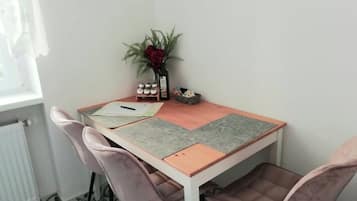 Un pequeño comedor con una mesa y cuatro sillas, un florero con flores, y un letrero en la pared que enumera los servicios de la habitación.