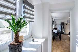 A modern interior with a potted plant on a windowsill, a dining area with a table and chairs, and a staircase leading to another level.