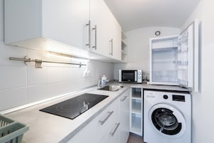 A modern kitchen with white cabinets, a built-in microwave, a washing machine, and a gas stove.