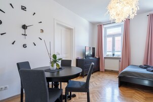 Una habitación moderna con una mesa redonda de comedor, dos sillas, un televisor, una cama y un reloj de pared grande.