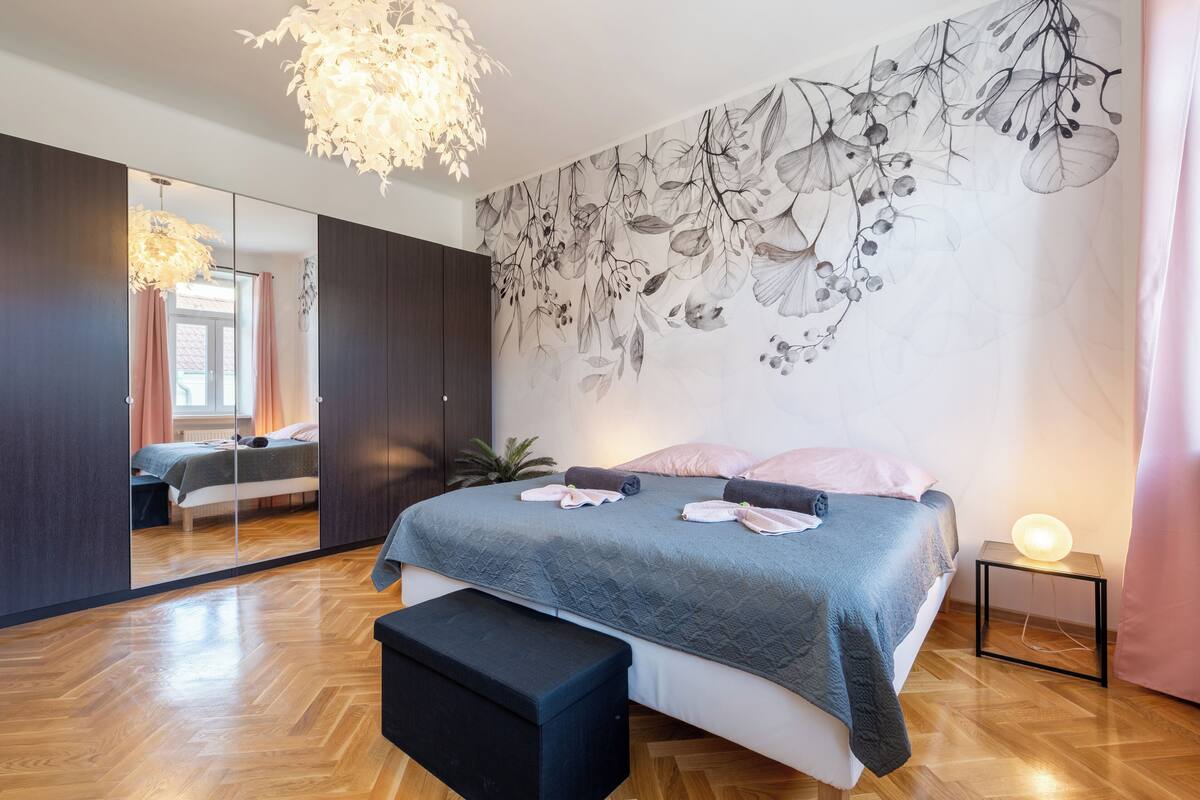 Ein Schlafzimmer mit einem großen Bett, einem Nachttisch mit Lampe, einem Spiegel und einer Wandmalerei.