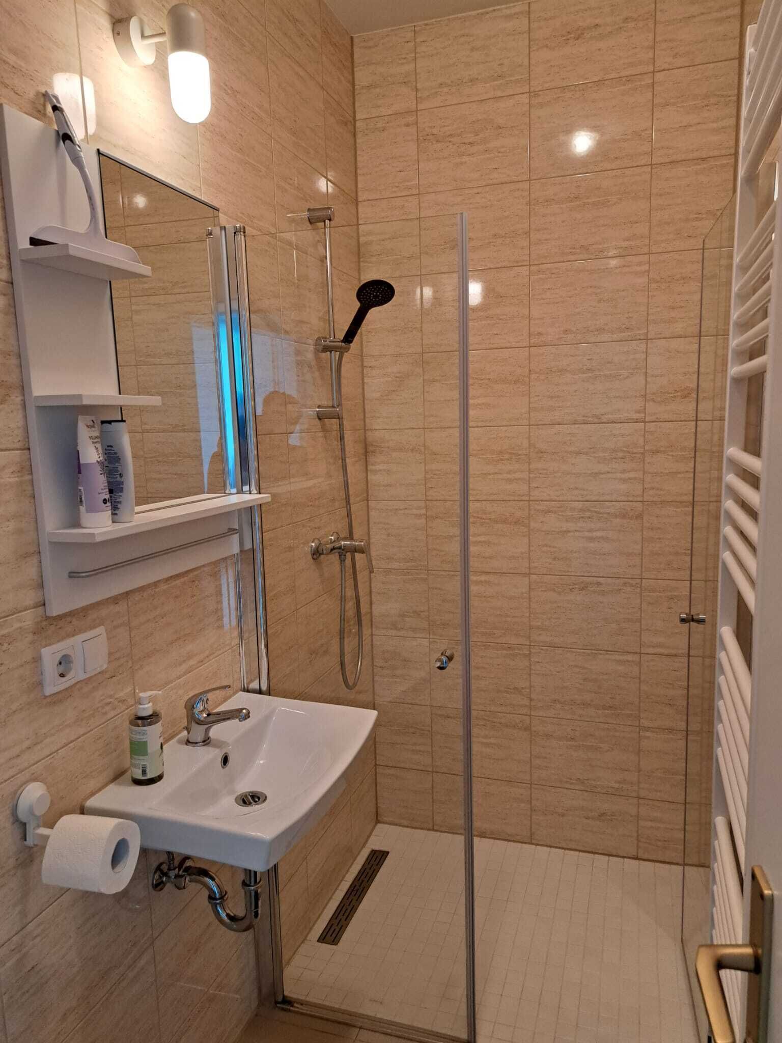 Un bany modern amb plat de dutxa de vidre, un lavabo amb mirall i una barra de tovalloles.