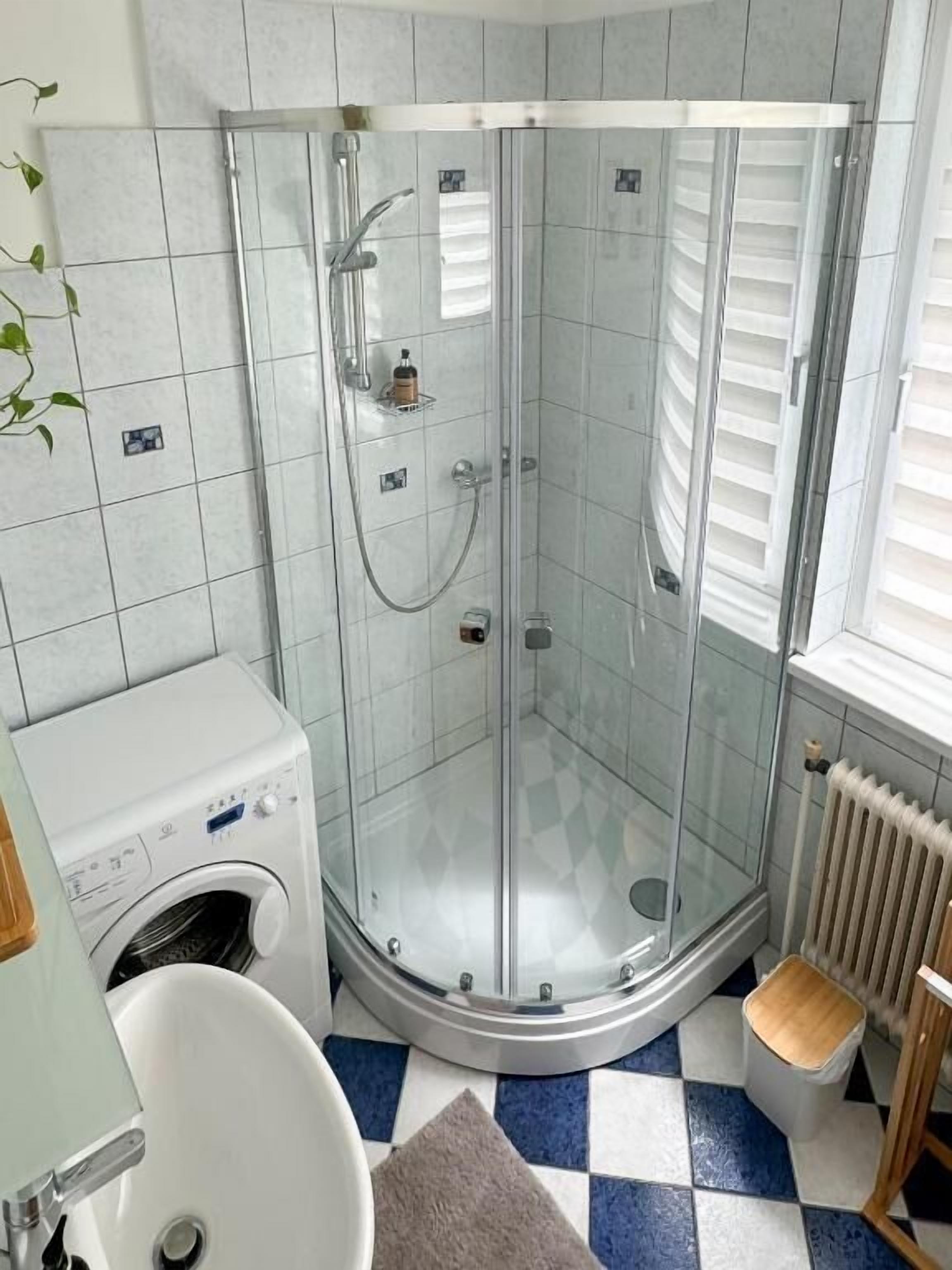 A bathroom with a glass-enclosed shower, a washing machine, a sink, and a radiator.