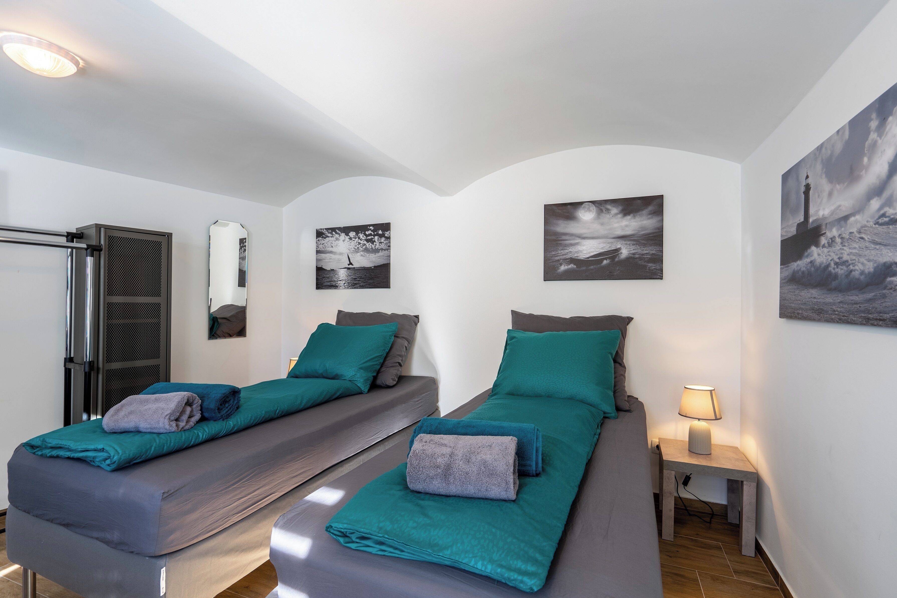 Une chambre double avec deux lits, chacun agrémenté de draps et d’oreillers de couleur turquoise, une petite table de chevet avec une lampe et des œuvres d’art accrochées aux murs.