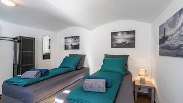 Une chambre double avec deux lits, chacun agrémenté de draps et d’oreillers de couleur turquoise, une petite table de chevet avec une lampe et des œuvres d’art accrochées aux murs.