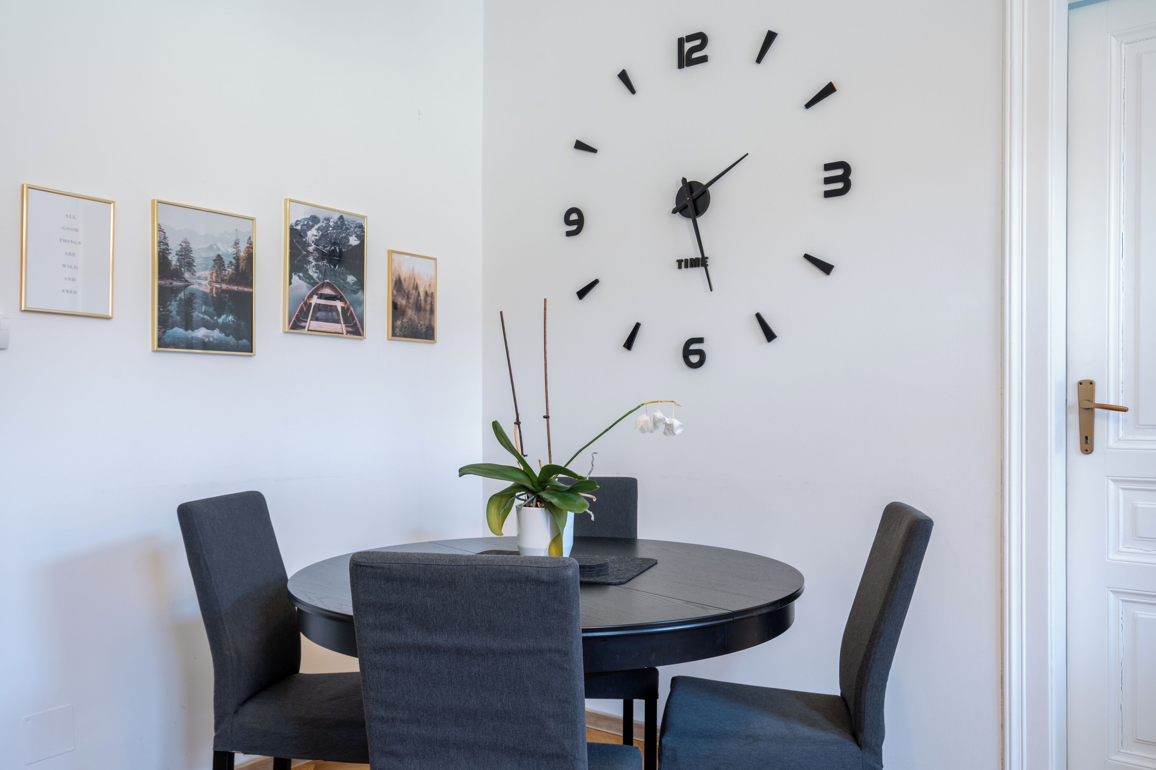 Un comedor con una mesa redonda, cuatro sillas, un reloj y tres cuadros en la pared.