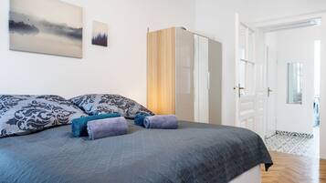 A neatly made bed with a grey quilt, two pillows with a black and white pattern, and two rolled towels in blue and purple.