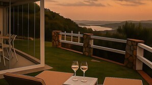 A patio with outdoor furniture and a table with two wine glasses, overlooking a scenic landscape with hills and a body of water. - Relaxation and comfort come together in an oasis of peace. Authentic Sardinia is waiting for you! (Porto Istana)