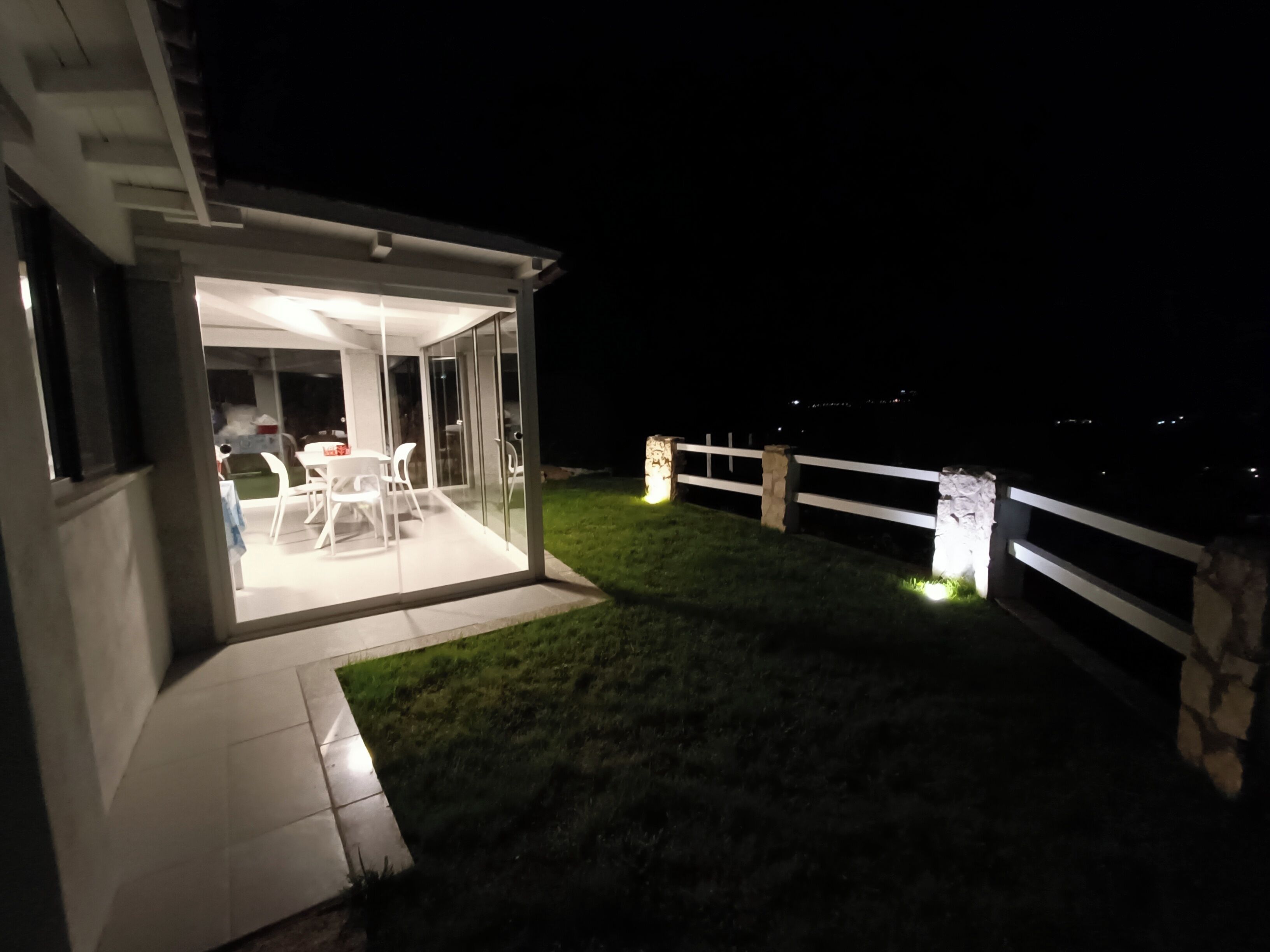 Een modern huis met een glazen patio, een witte hek en een verzorgd gazon.