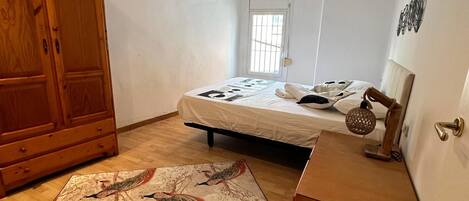 A bedroom with a bed, a ceiling fan, a wooden wardrobe, a door, and a window.