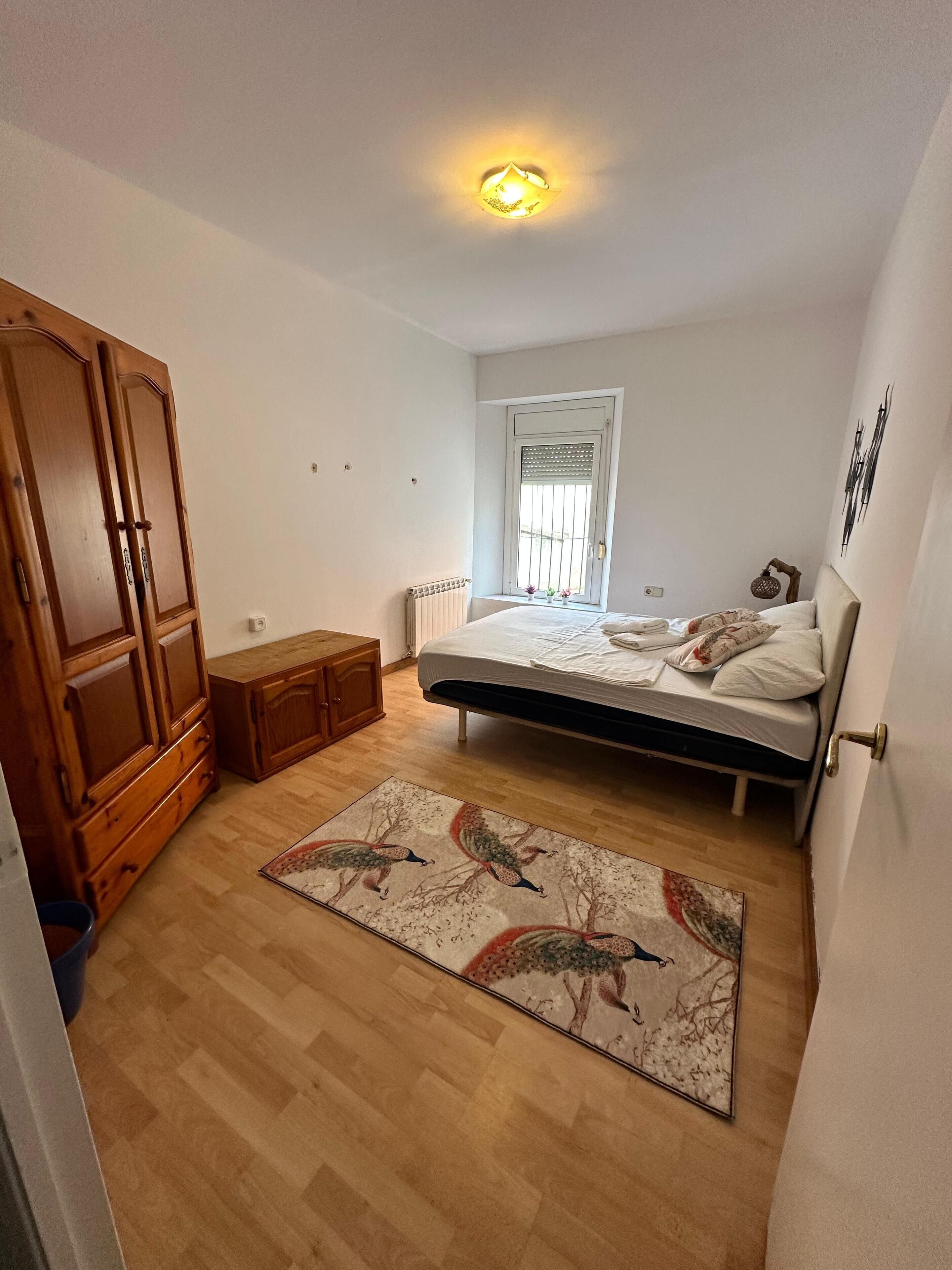 A bedroom with a bed, wooden wardrobe, and a radiator.