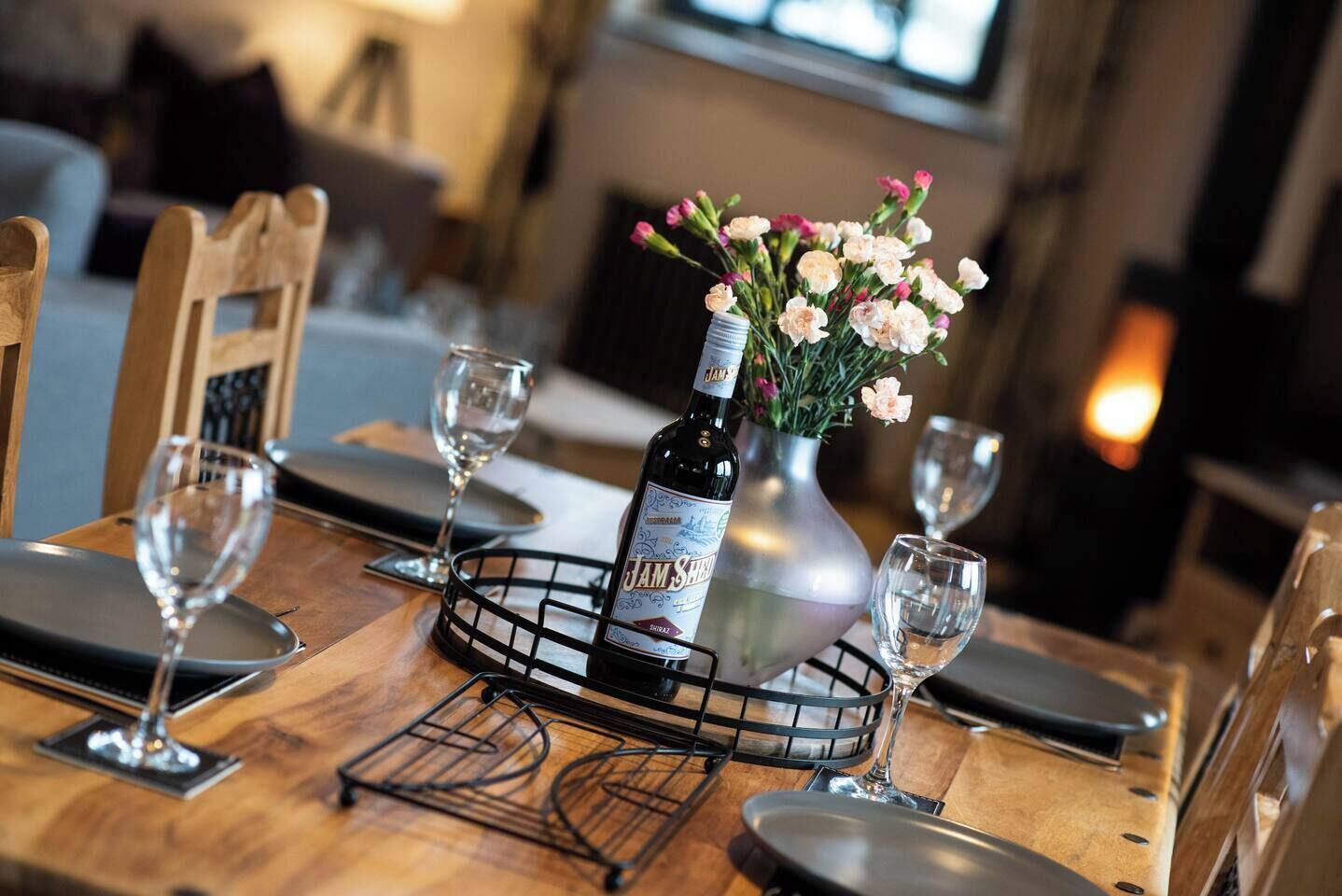 Une table à manger dressée avec des verres à vin, une bouteille de sherry et un vase rempli de fleurs.