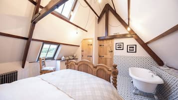 Une chambre avec un grand lit, une tête de lit en bois, une fenêtre, une armoire en bois, une baignoire blanche et des carreaux décorés.
