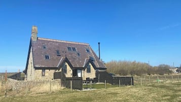 Une grande maison en pierre à deux étages, dotée d’un toit en pente et de nombreuses fenêtres.