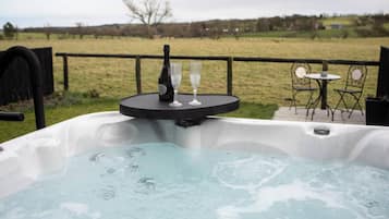 Un bain à remous avec une table et des chaises en arrière-plan, entouré d’une clôture et d’un champ d’herbe.