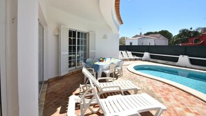 Une terrasse avec une piscine, des meubles blancs et une table dressée pour le repas.