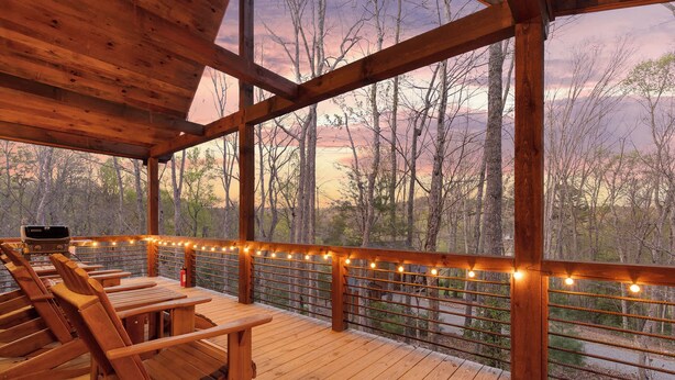 Una terraza de madera con asientos y luces colgantes, con vista a un área boscosa.
