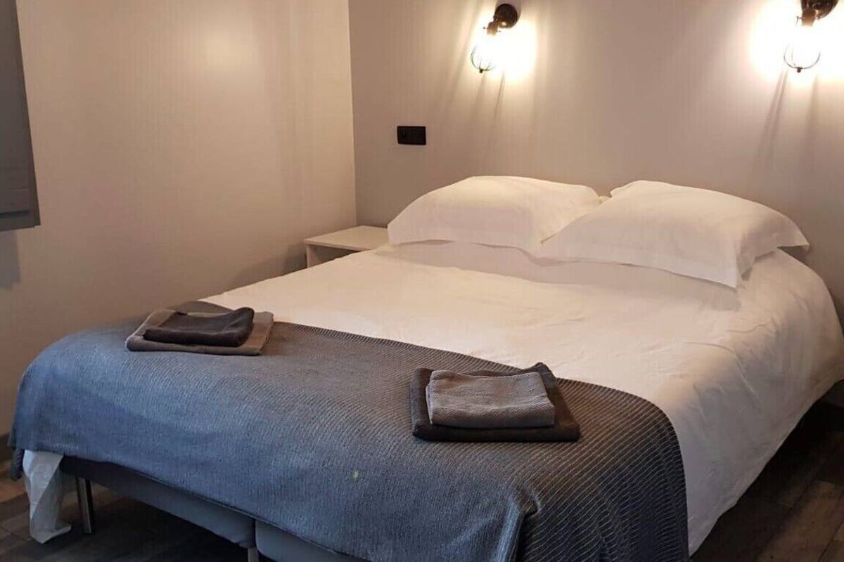 A neatly made bed with white linens, two bedside tables, and a wall-mounted light fixture.