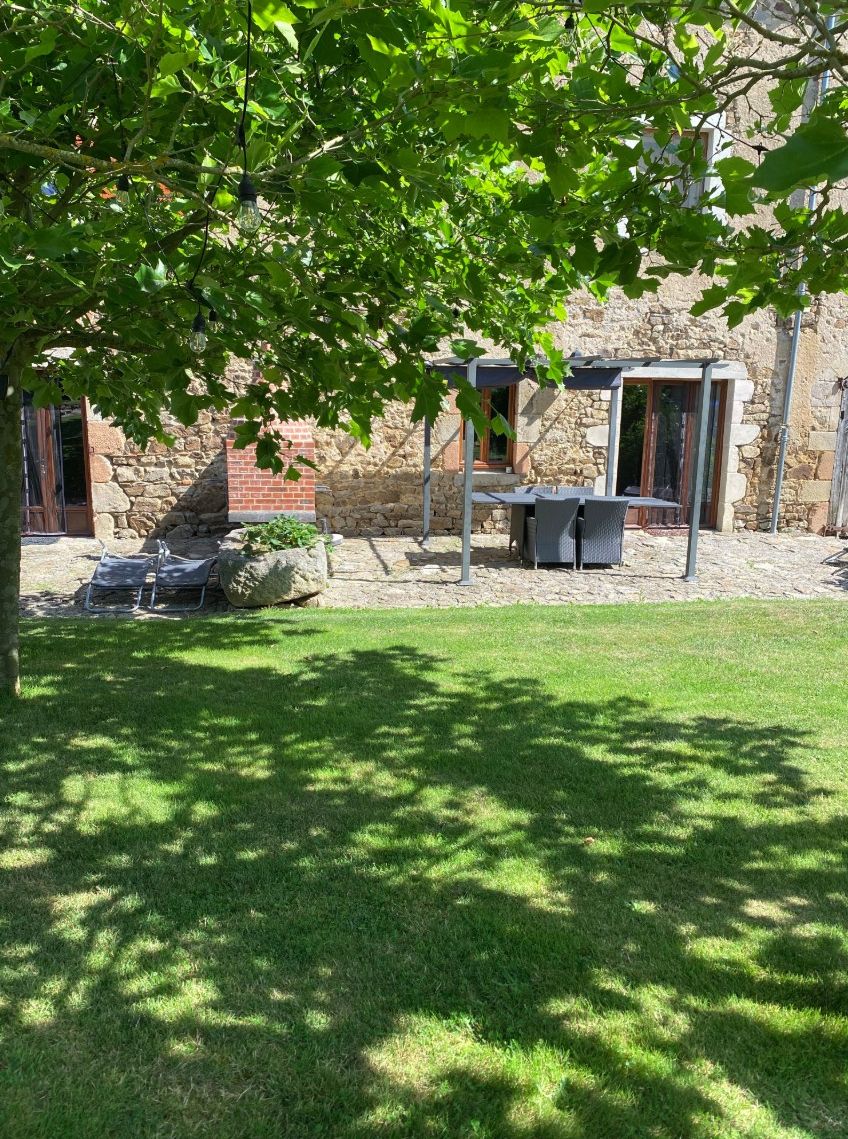 Un edificio de piedra con un patio, mobiliario exterior y césped.
