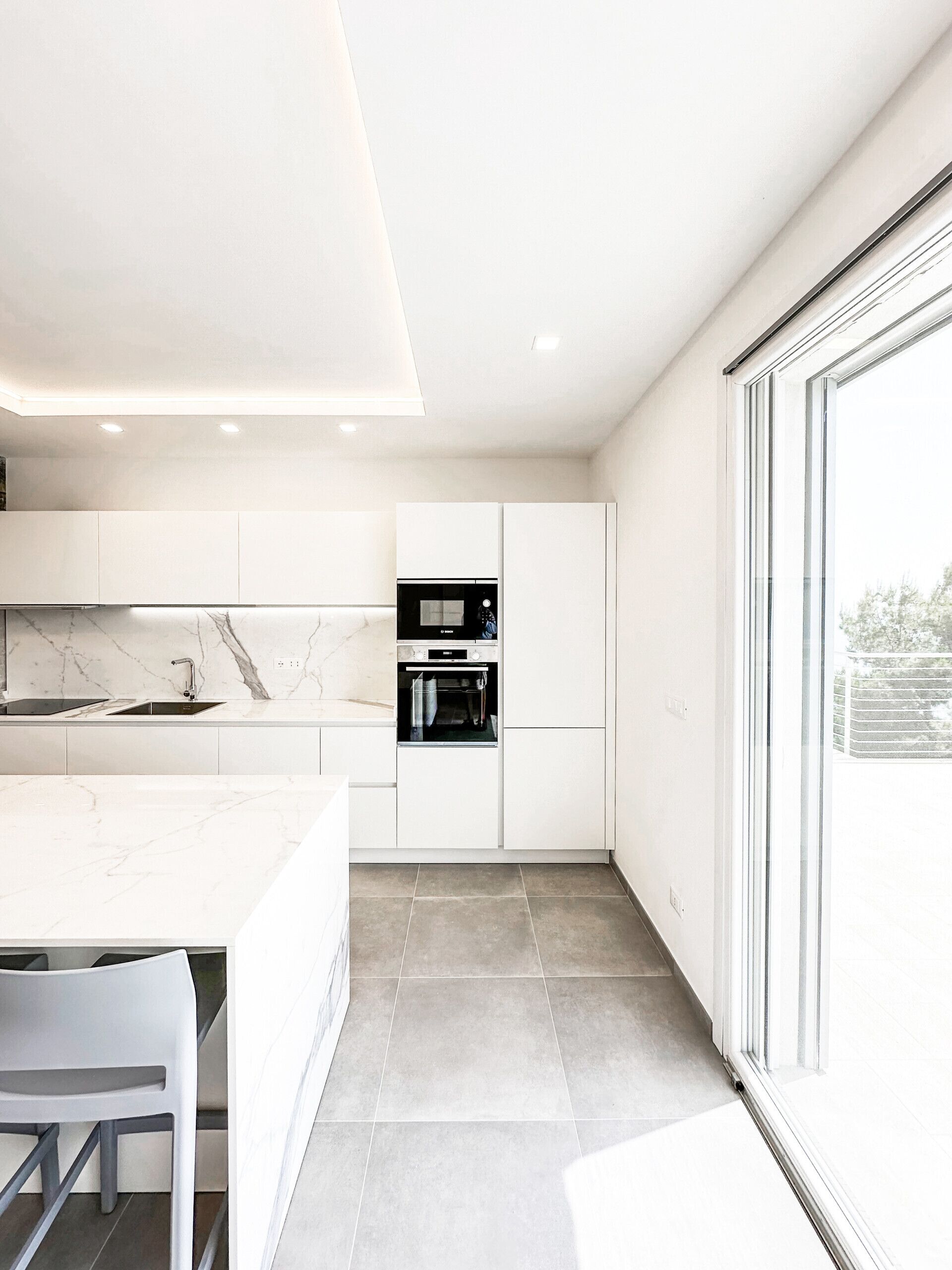 Una cocina moderna con muebles blancos, salpicadero de mármol y horno empotrado.