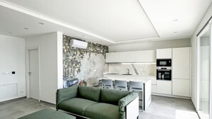 A modern living room with a green sofa, a dining area with a white table, and a kitchen with white cabinets and appliances. - Orizzonti Blu Pool Villa by Wonderful Italy (Cervo)