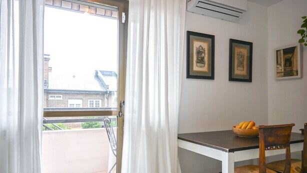 Una habitación con balcón, una mesa con frutero y dos cuadros en la pared.