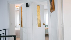 Un pasillo con puertas blancas, una de ellas con un panel decorativo dorado. A la derecha, hay un cuadro enmarcado en la pared.