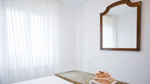 Habitación de hotel con cama, mesita de noche de piedra con toallas dobladas, espejo grande y cortinas de gasa.