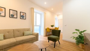 A modern living room with a beige sofa, two round wooden tables, a green armchair, and a dining area with yellow chairs.