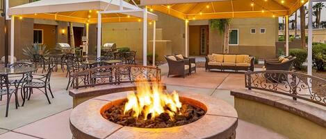 An outdoor patio with a fire pit, seating areas, and umbrellas providing shade.