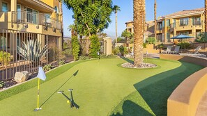 A mini-golf course with a flagstick, putting mat, and golf club.