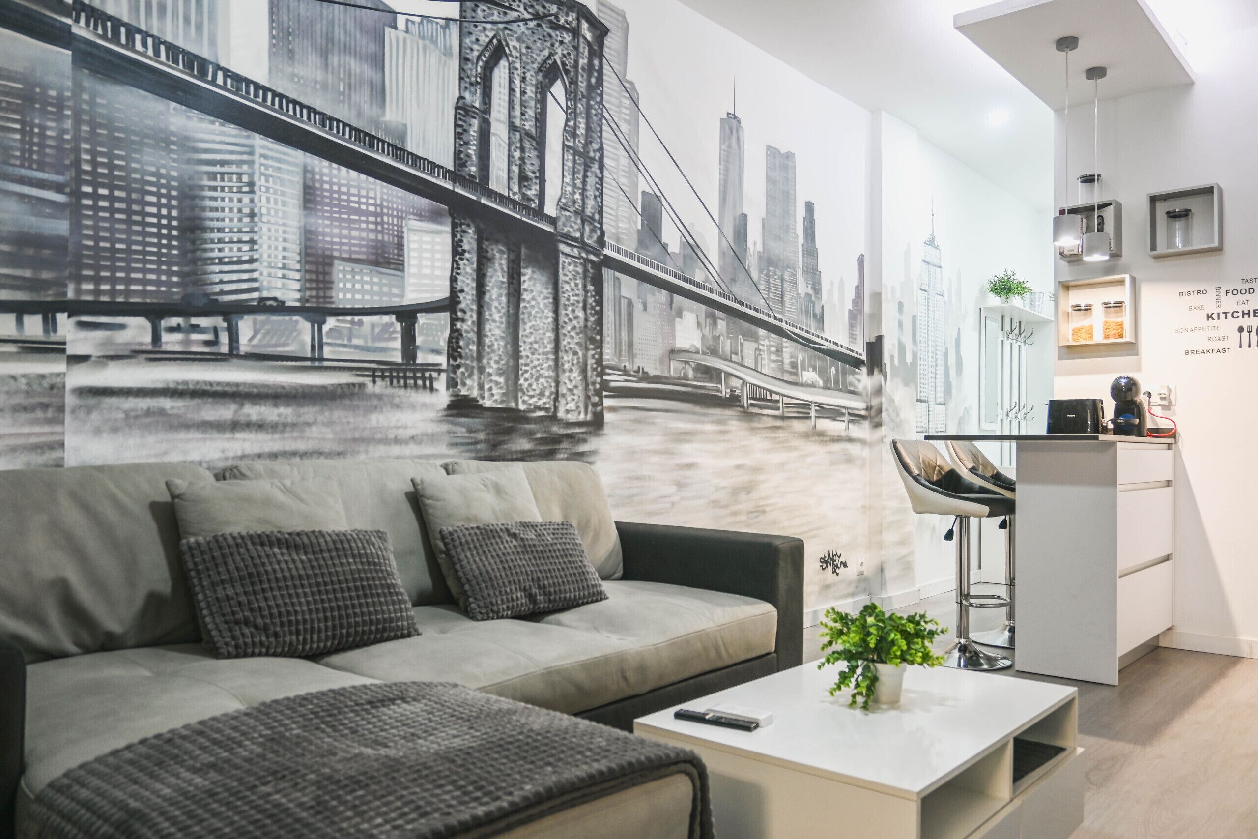 A modern living room with a sofa, coffee table, and a mural of a cityscape.