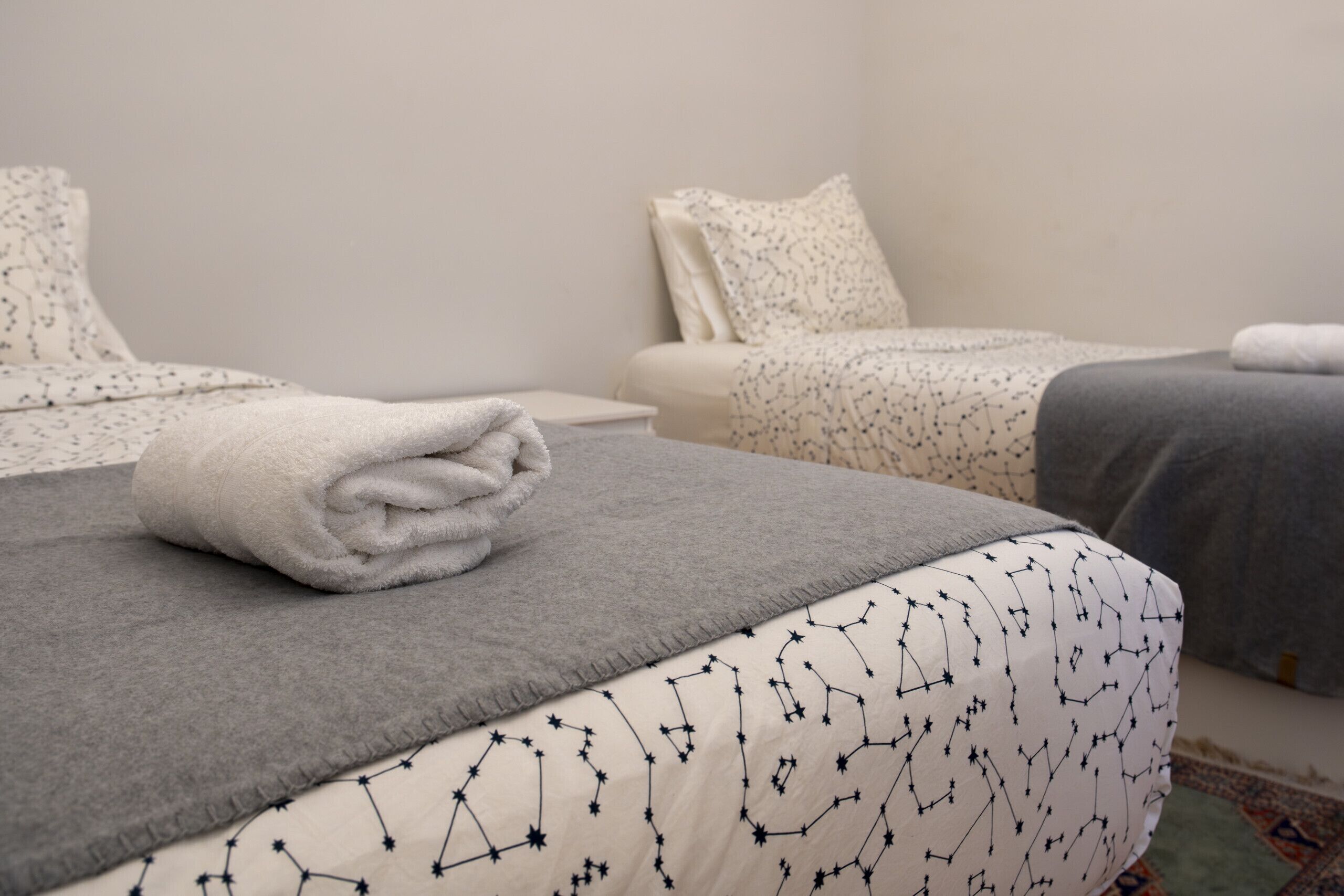 Una cama bien hecha con un edredón gris y una almohada blanca con un diseño de estrellas.