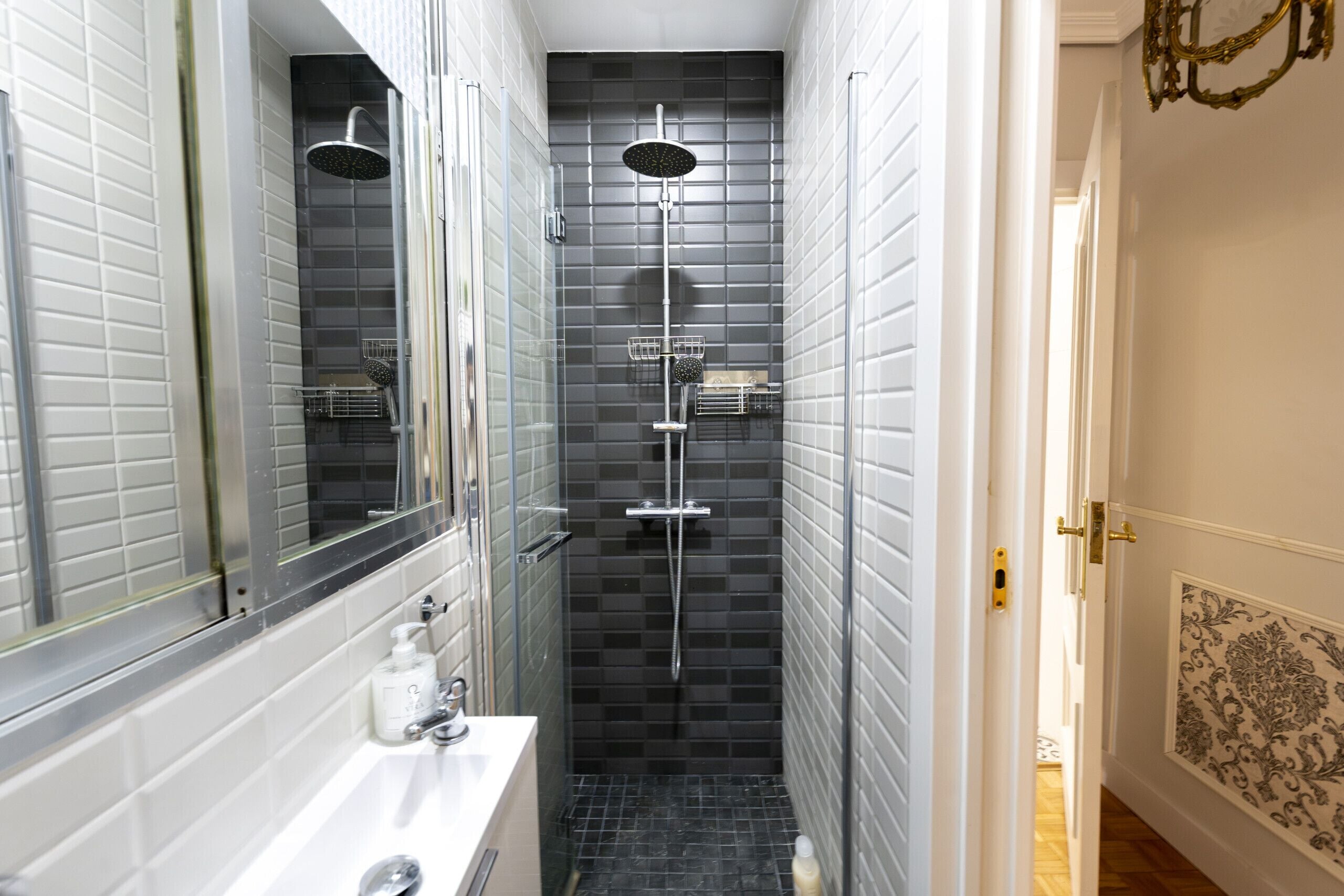 Un baño estrecho con ducha, lavabo y espejo.