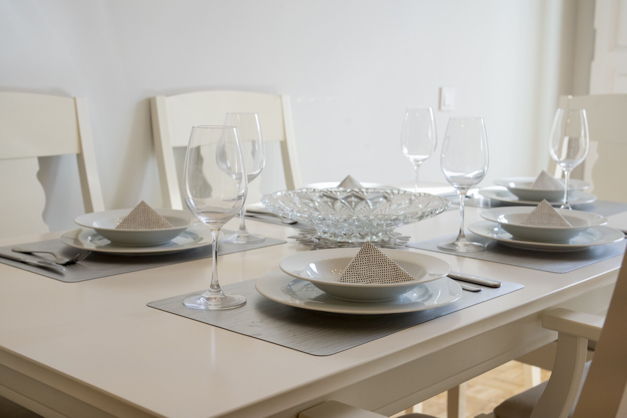 A dining table set with white plates, clear glasses, and a decorative glass bowl.