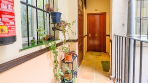 Un pasillo con puerta de madera, baranda metálica y plantas en macetas sobre una estantería.