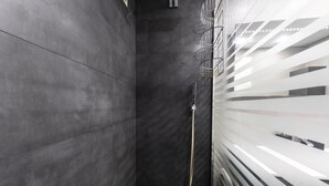 A modern bathroom with dark tiles, a glass shower enclosure, and a metal showerhead.