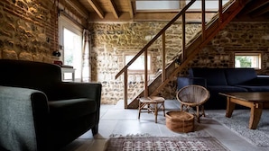 A rustic interior with a stone wall, wooden staircase, and a cozy seating area with a sofa and chairs.