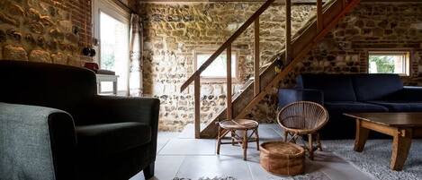 A rustic interior with a stone wall, wooden staircase, and a cozy seating area with a sofa and chairs.