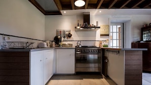 A compact kitchen with white cabinets, a stainless steel oven, and a hanging pot rack.